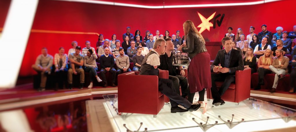 René Schaar im Fernsehstudio von stern TV, während er neben dem Moderator Steffen Hallaschka sitzt und geschminkt wird.