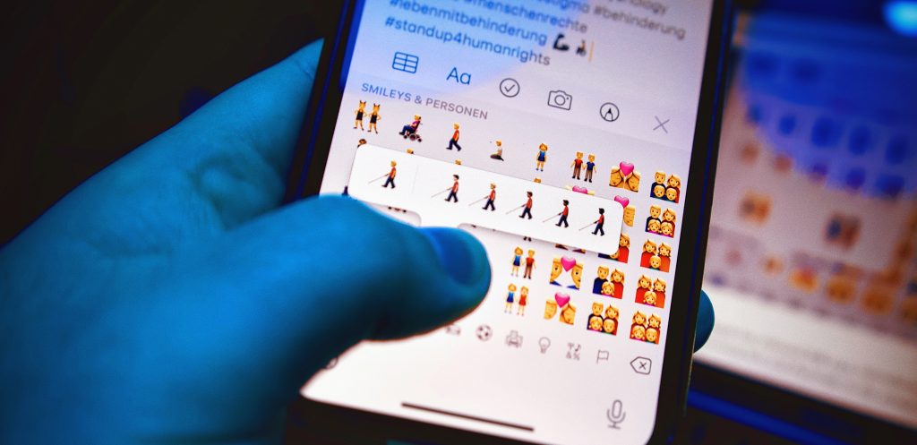 Ein Finger sucht auf einer Smartphone-Tastatur nach neuen Emojis, die Menschen mit Behinderung zeigen.